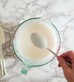 a hand holding a spoon over a bowl of milk on top of a marble counter