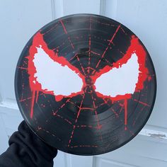 a person holding up a black and red record with white paint on it's face