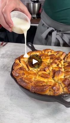 a person pouring milk on top of a baked pastry in a cast iron skillet