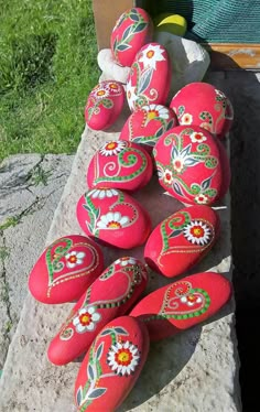 a group of red painted rocks sitting on top of a cement slab next to grass