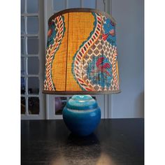 a blue vase sitting on top of a table under a lampshade with a yellow shade