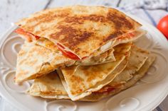 a stack of quesadillas on a white plate with tomatoes in the background