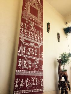 a red and white wall hanging next to a potted plant