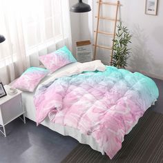 a bed with pink and blue comforters in a room next to a white table