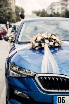 a blue car is decorated with flowers and a white ribbon on the hood for a wedding ceremony