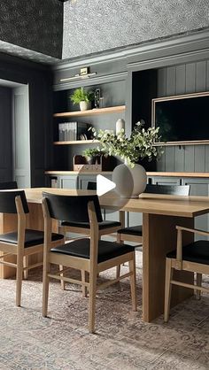 a dining room table with black chairs and shelves on the wall in front of it