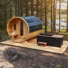 a wooden barrel sauna in the woods next to a bench and hot tub on a platform