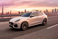 a white masera is driving down the road in front of a cityscape