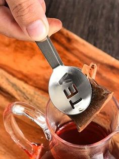 a person is holding a spoon over a cup of tea with the letter e on it