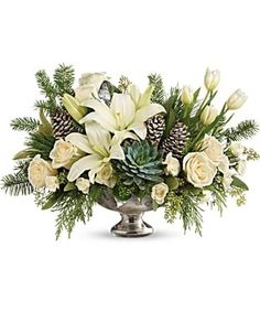 a silver vase filled with white flowers and pine cones on a white background, surrounded by greenery