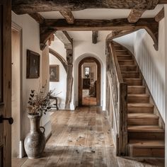 a hallway with wooden floors and stairs leading up to the second floor, along with a vase filled with flowers