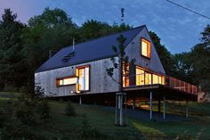 a house that is in the middle of some grass and trees at night with windows lit up