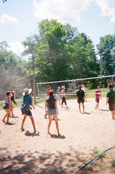 a group of young people playing volleyball on a sandy court with trees in the background