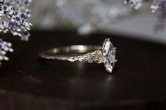 a close up of a diamond ring on a table with flowers in the back ground