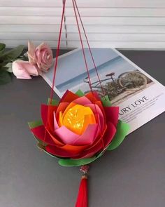 an origami flower hanging from a red string with a tassel on it