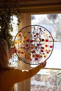 a woman holding up a glass plate with flowers on it in front of a window