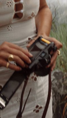 a woman in white dress holding a camera with strap around her waist and wearing gold rings