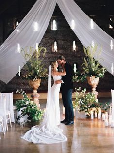 a bride and groom kissing in front of an altar with flowers, candles and greenery