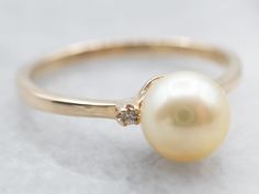 a pearl and diamond ring sitting on top of a white surface with a gold band