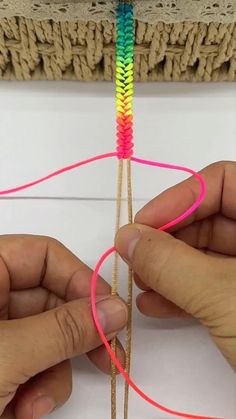 two hands are working on an object with colored thread and yarn in the shape of a heart