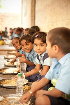 several children are sitting at a long table with plates of food in front of them