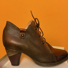 a pair of brown leather shoes sitting on top of a white box next to an orange wall