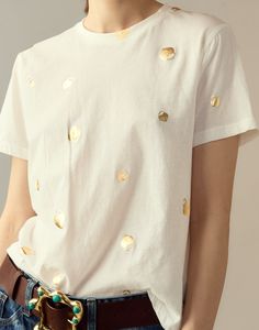 a woman wearing a white shirt with gold dots on it