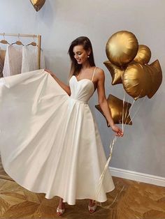 a woman in a white dress is holding some gold balloons and posing for the camera