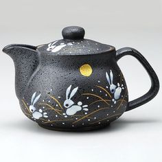 a black tea pot with white rabbits painted on it