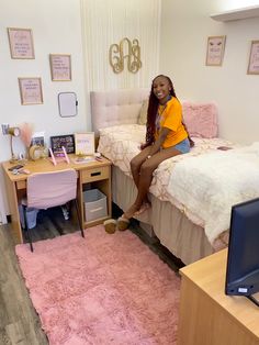 a woman sitting on top of a bed next to a desk with a computer monitor