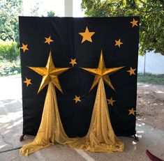 three gold stars on black backdrop in front of trees