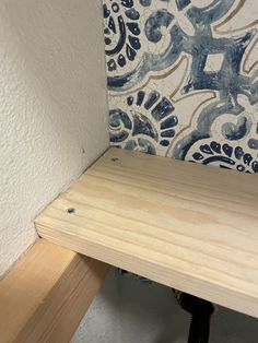 a wooden shelf sitting in front of a wall with blue and white tiles on it