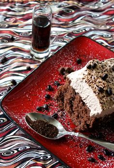 a piece of cake on a red plate next to a spoon with chocolate chips and sprinkles