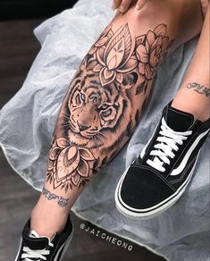 a woman's leg with a tiger tattoo on it and flowers around her ankles