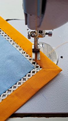 a close up of a sewing machine on a piece of fabric with an orange and blue border