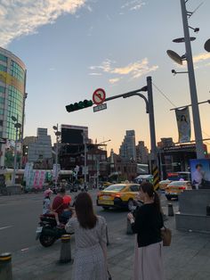 two women are walking down the street in front of some traffic lights and buildings at sunset