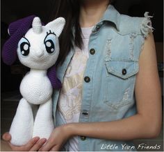 a woman holding a white stuffed animal with big eyes and a purple hat on her head