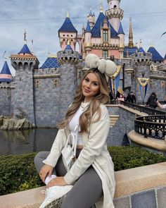 a woman sitting on top of a stone wall in front of a castle with turrets