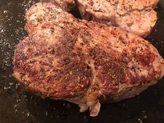 two steaks cooking in a skillet with seasoning on top and the meat being cooked