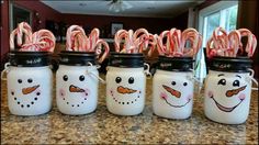 some jars with candy canes and snowman faces painted on them sitting on a counter