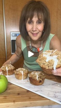 a woman holding a muffin in front of some other muffins on a cutting board