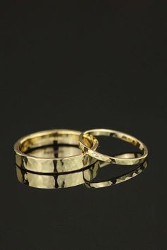 two gold wedding rings sitting next to each other on a black surface with reflection in the middle