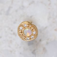 an opal and diamond ring sits on a marble surface in front of a white background