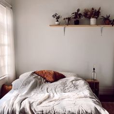 an unmade bed with plants on the shelves above it