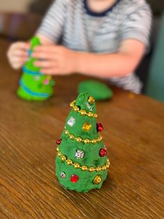 a small green christmas tree sitting on top of a wooden table next to a little boy