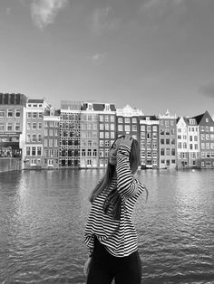 black and white photograph of woman in front of water with buildings on the other side