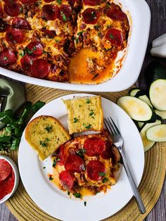 a pizza casserole on a plate next to bread and sliced cucumbers