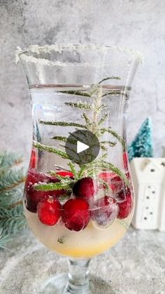 a glass filled with liquid and berries sitting on top of a marble table next to evergreen branches