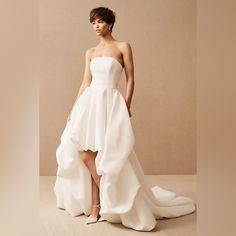 a woman in a strapless white wedding dress with high low heels standing against a beige background