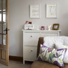 a white dresser sitting next to a brown couch in a room with pictures on the wall